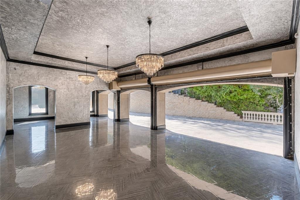 Open interior room with polished tile floors, chandeliers, and a wide doorway to a terrace.