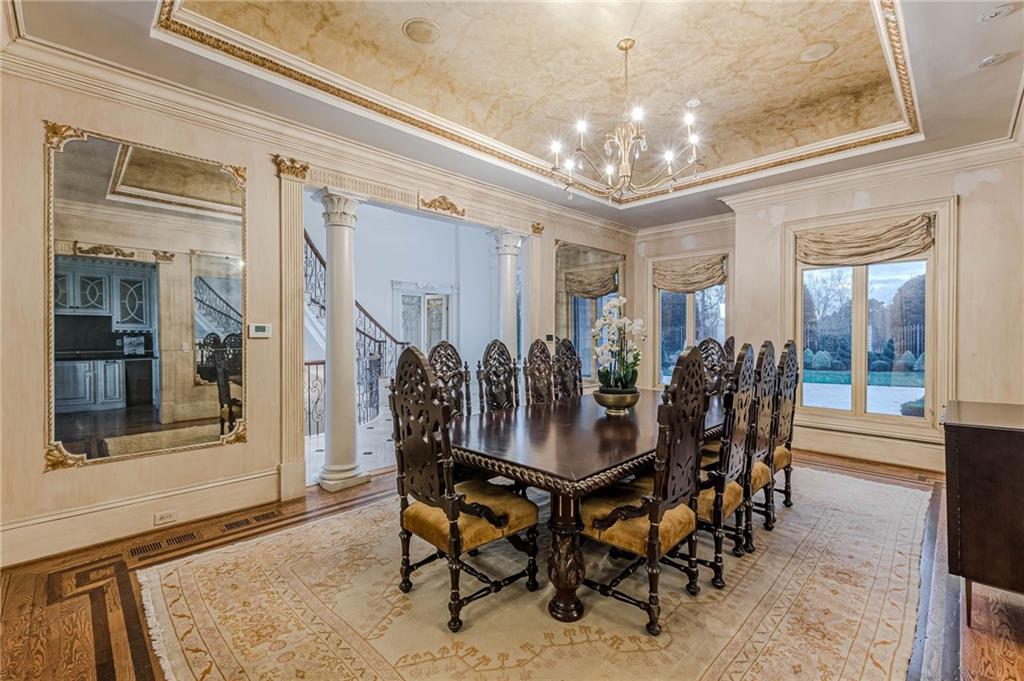 Formal dining room with a carved wood table, ornate ceiling, chandelier, and tall windows.