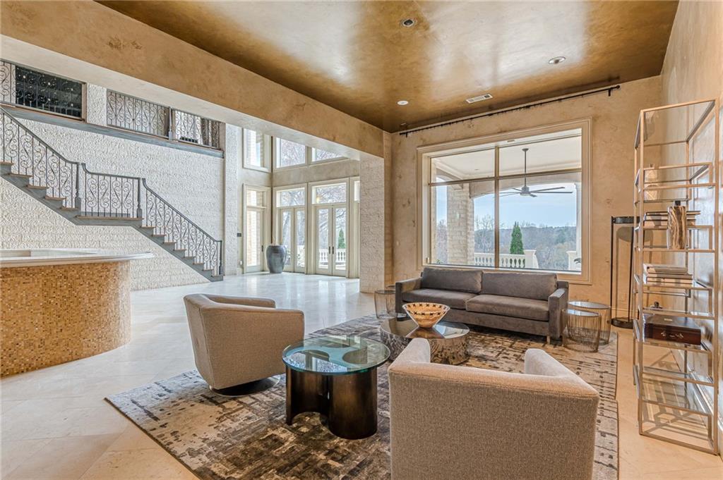 Living room with a sweeping iron-railed staircase, high wood ceiling, and large windows.