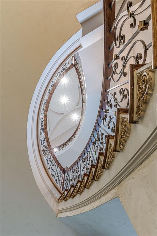 Curved staircase with ornate wrought-iron railings and bright ceiling lights.