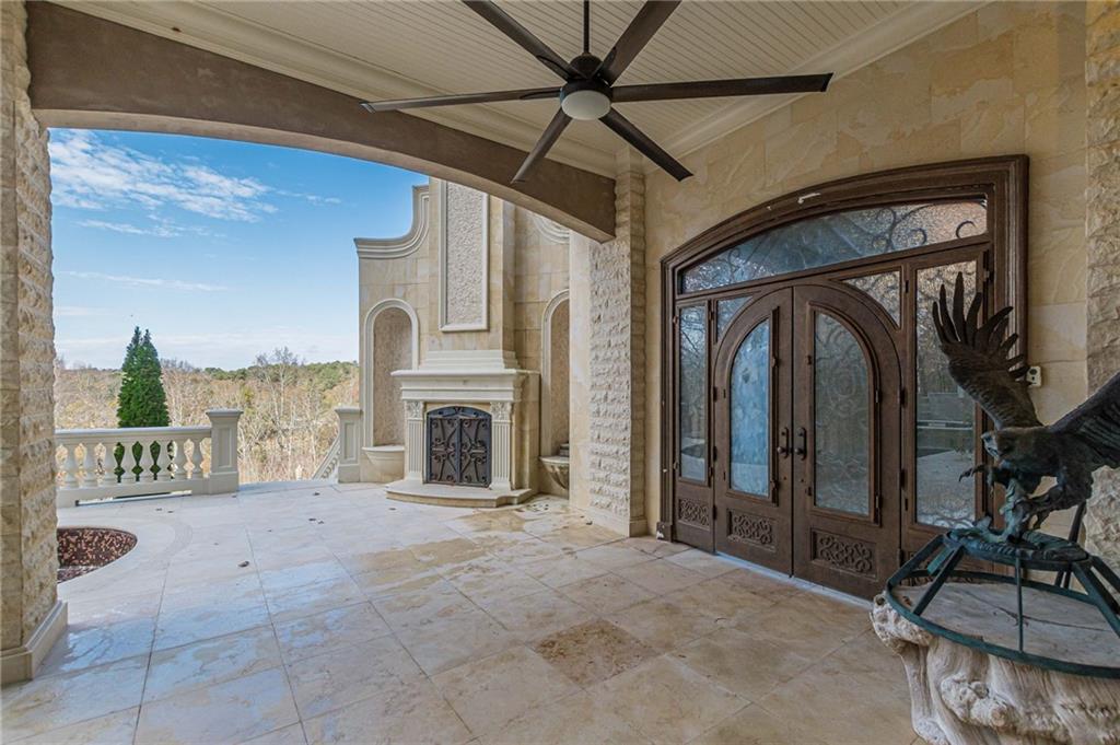 Covered stone patio with ornate double doors, a fireplace, and a wooded view.