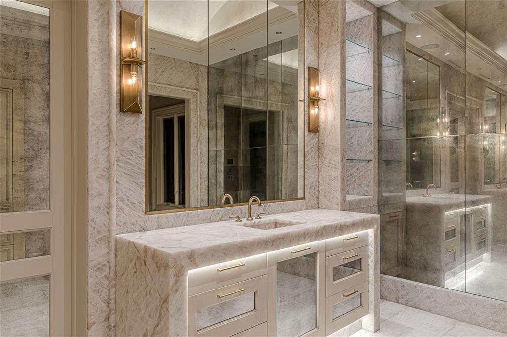 Marble bathroom with an illuminated vanity, brass fixtures, and a glass-enclosed shower.