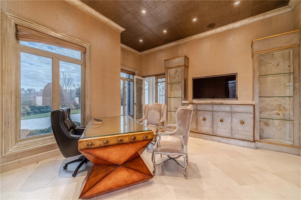 Furnished home office with a sculptural desk, built-in cabinetry, and large windows overlooking the yard.
