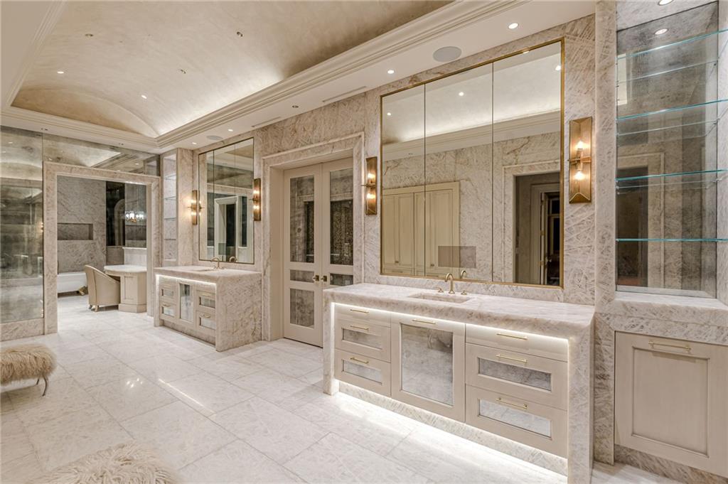 Marble bathroom with two illuminated vanities, large mirrors, and glass display shelves.