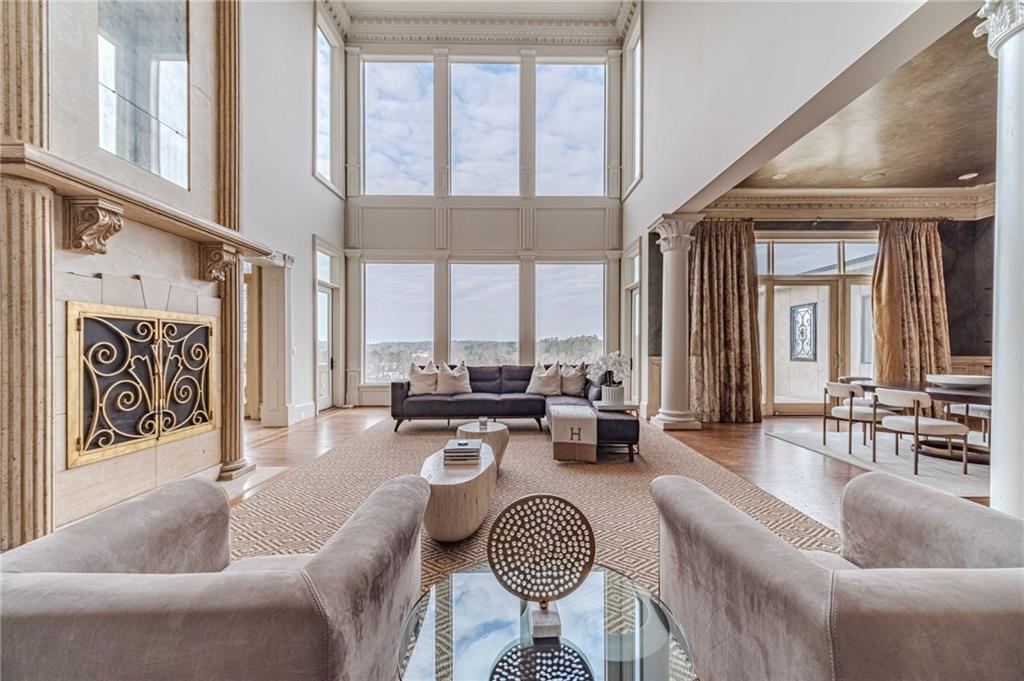 Double-height living room with a stone fireplace, tall windows, and neutral seating.