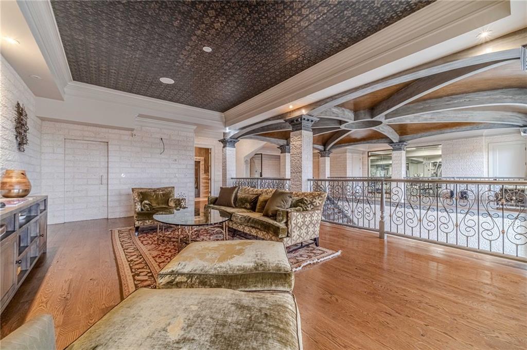 Living room with hardwood floors, patterned rug, sectional seating, and ornate beamed ceiling beside an iron railing.