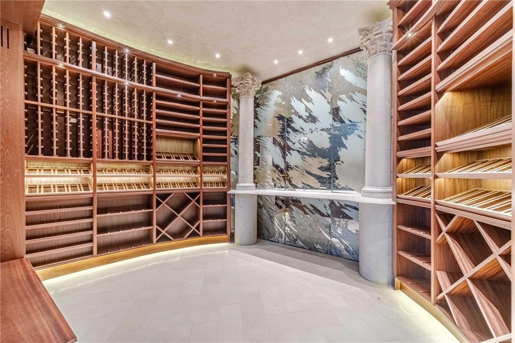 Wine cellar with curved wood wine racks, decorative stone wall panels, and white columns.