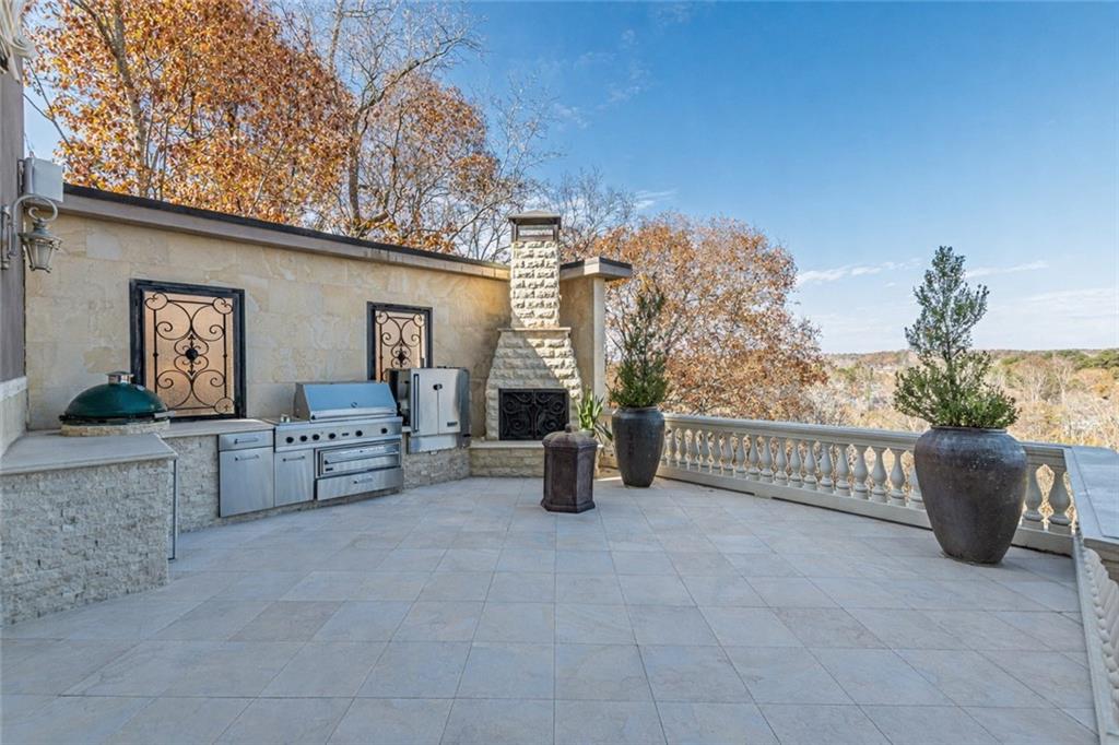 Stone-tiled terrace with an outdoor grill and fireplace overlooking autumn trees.