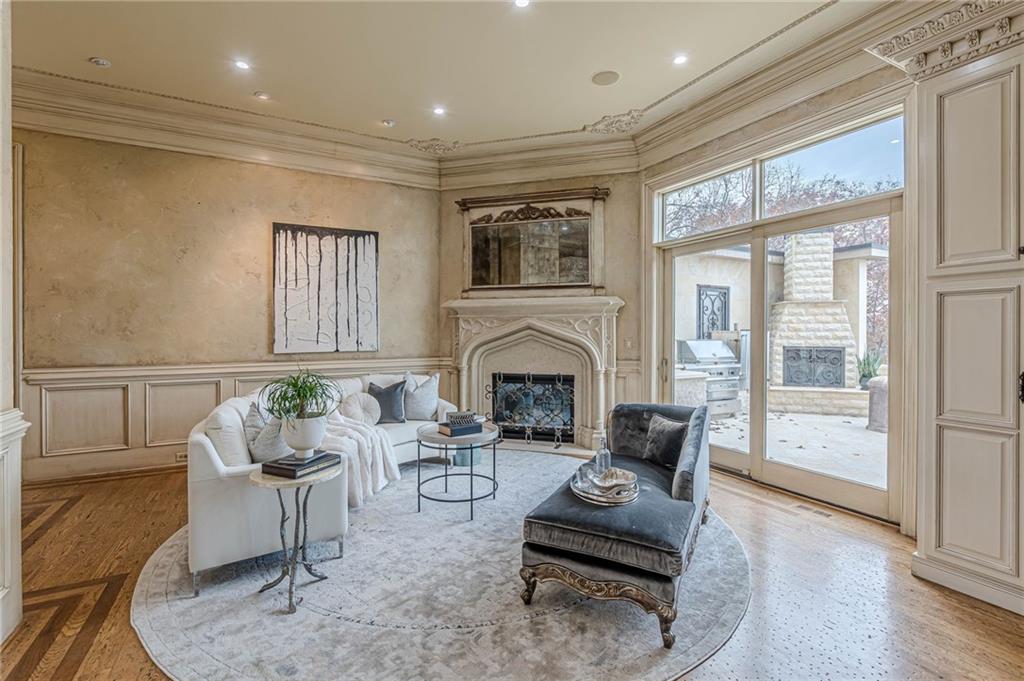 Living room with an ornate fireplace, hardwood floors, and tall doors opening to a stone patio.