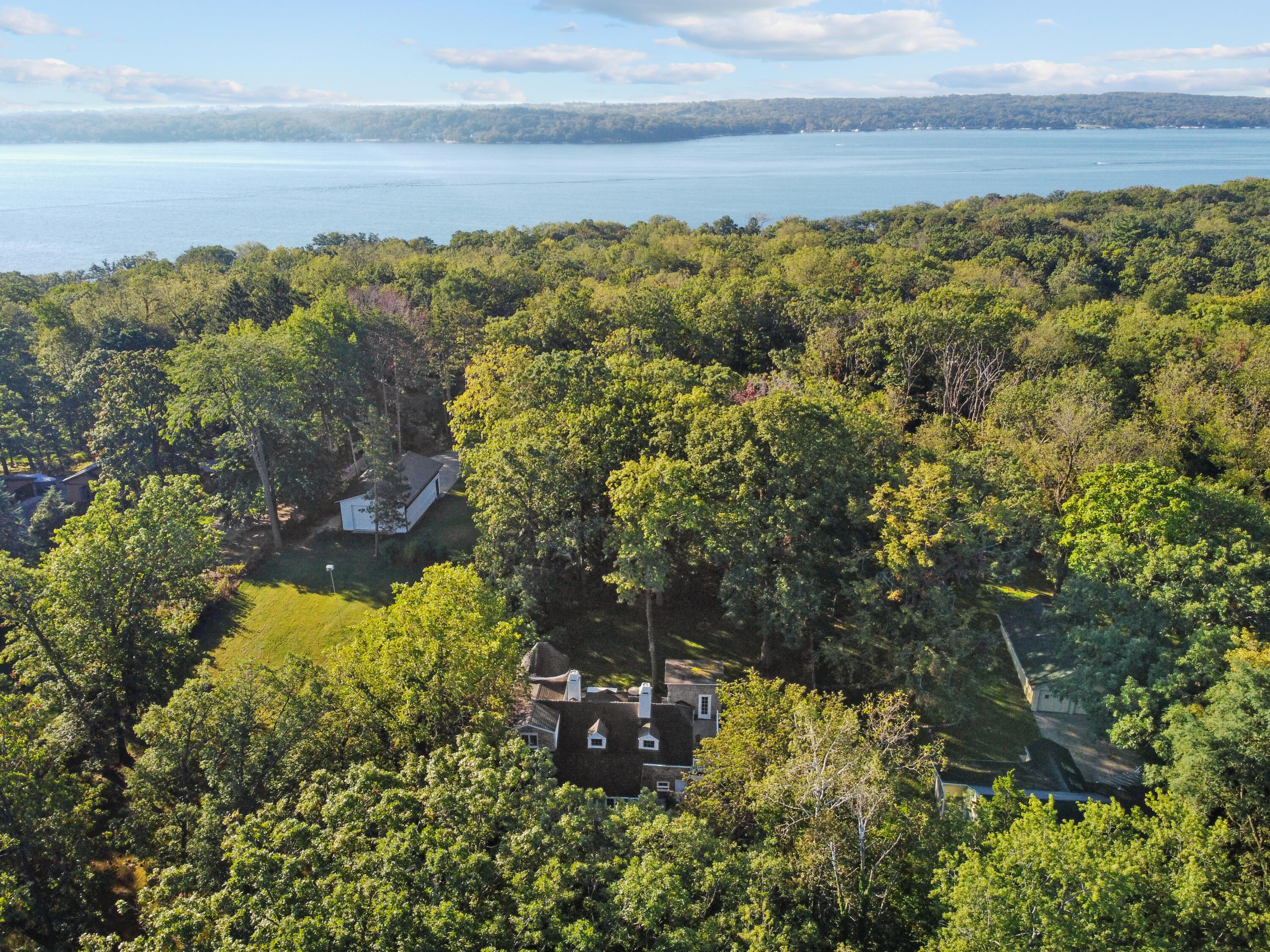 Aerial view of a wooded home with a lake and distant tree-lined shore beyond.