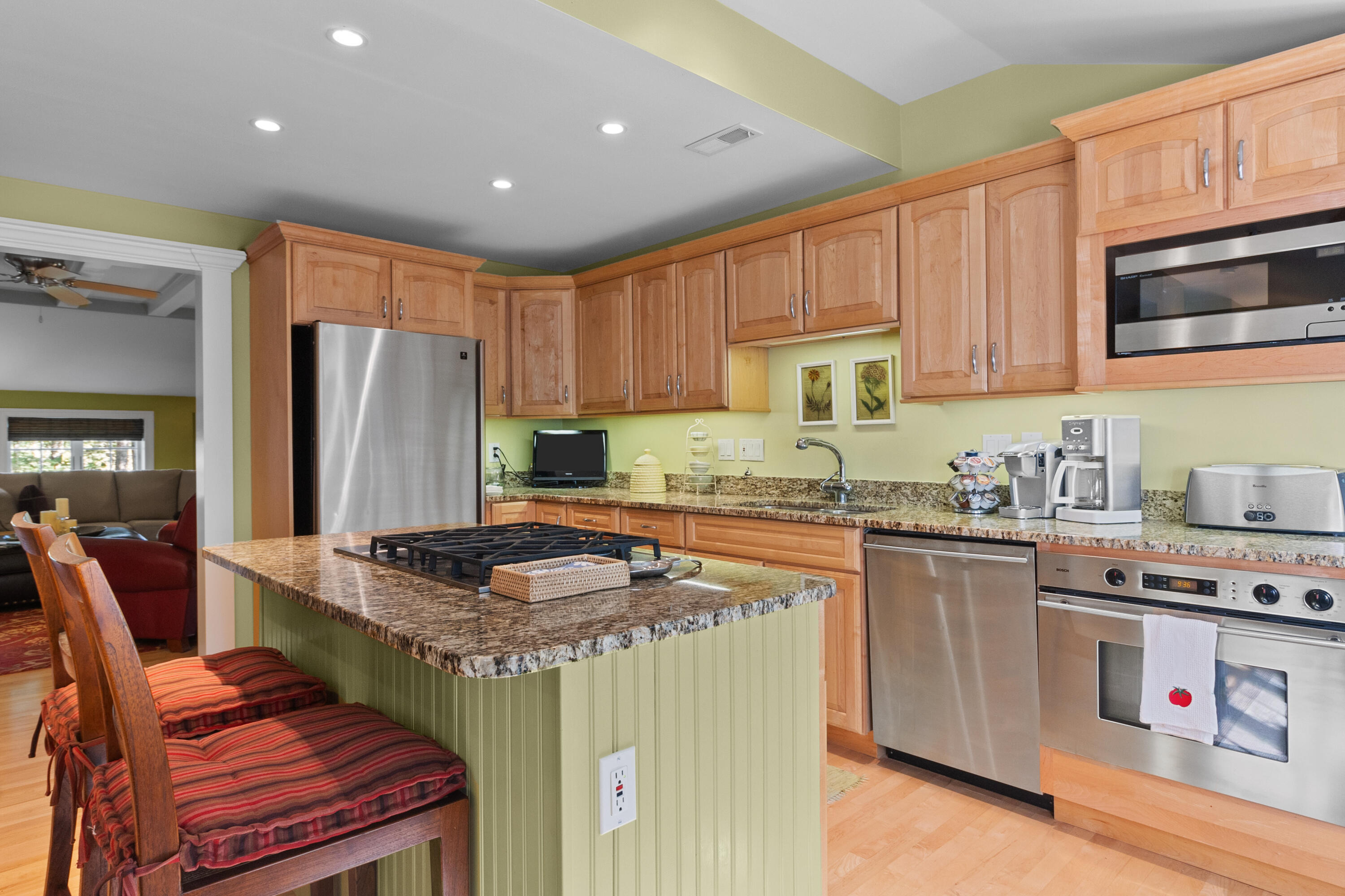 Kitchen with granite island and gas cooktop, honey-colored cabinets, and stainless-steel appliances.