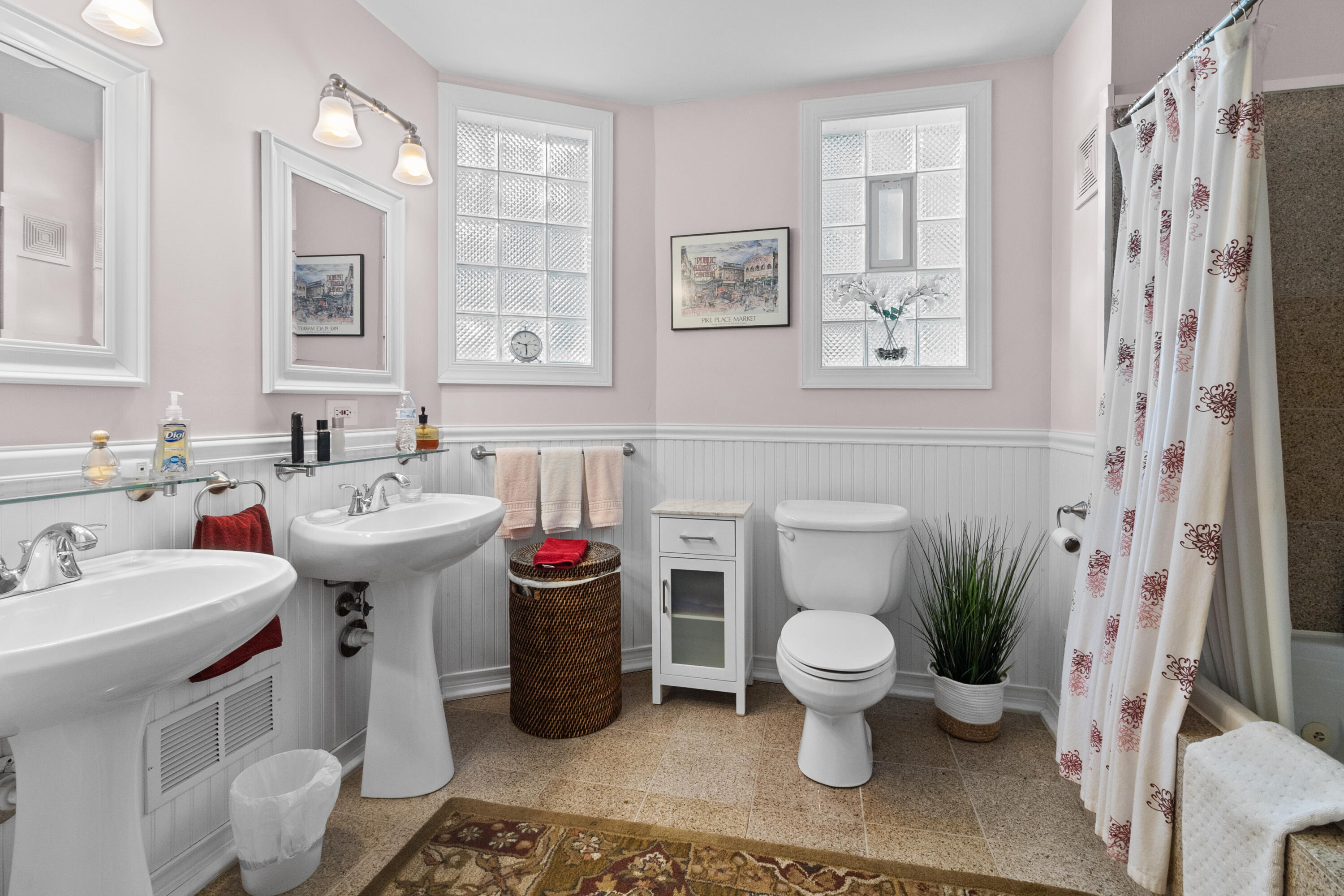 Bathroom with two pedestal sinks, glass-block windows, white beadboard, and a patterned shower curtain.
