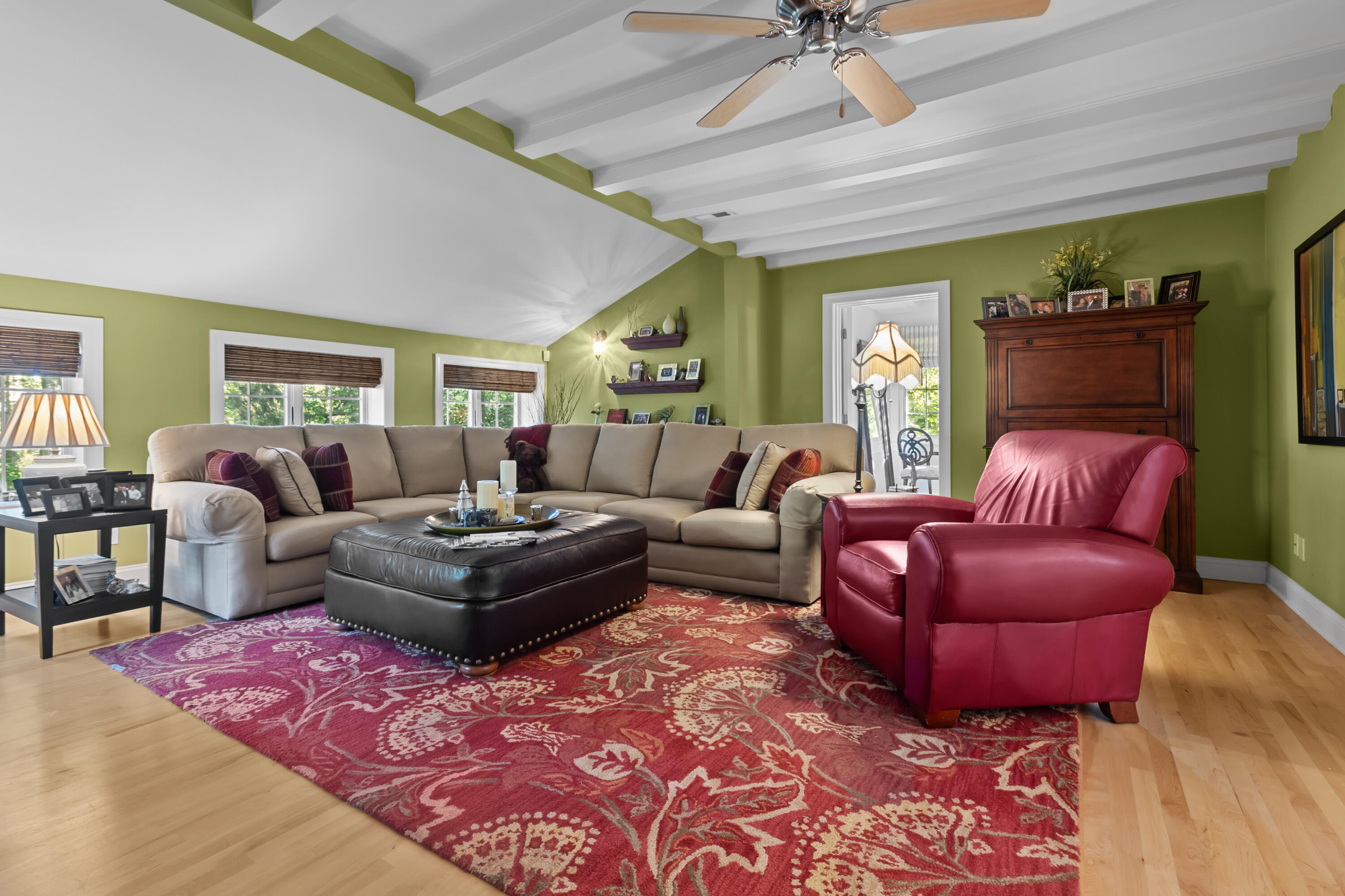 Living room with a beige sectional, red leather armchairs, and a white exposed-beam ceiling.