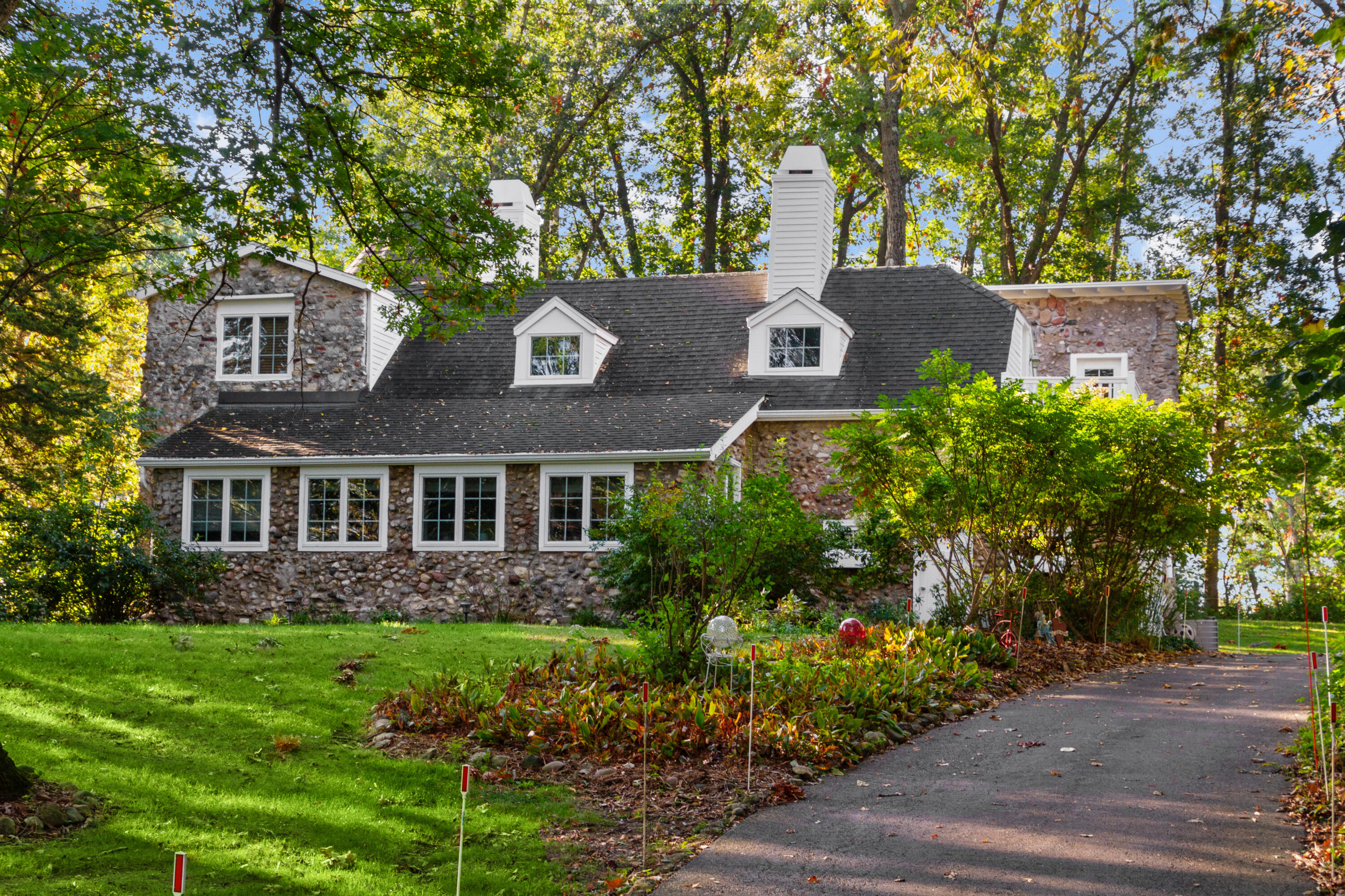 Stone house with white dormers and chimneys, framed by mature trees and landscaped gardens.