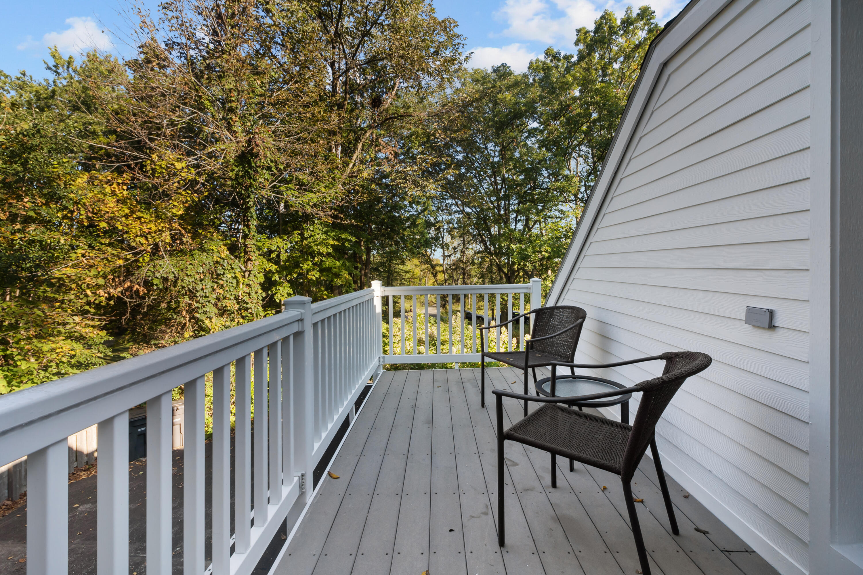 Raised deck with white railings and two woven chairs overlooking leafy trees.