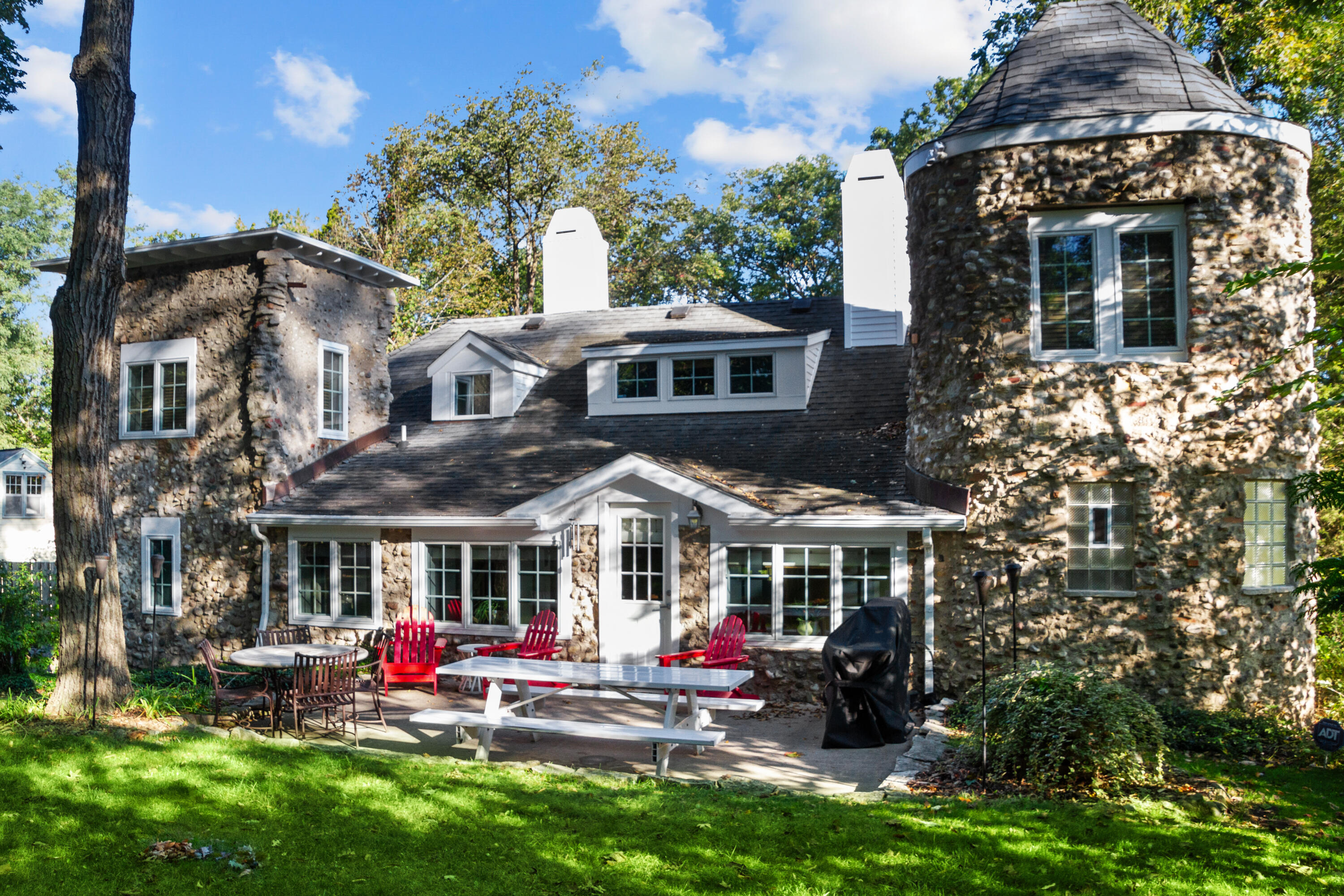 Stone house with a round turret and patio furnished with red Adirondack chairs and picnic tables.