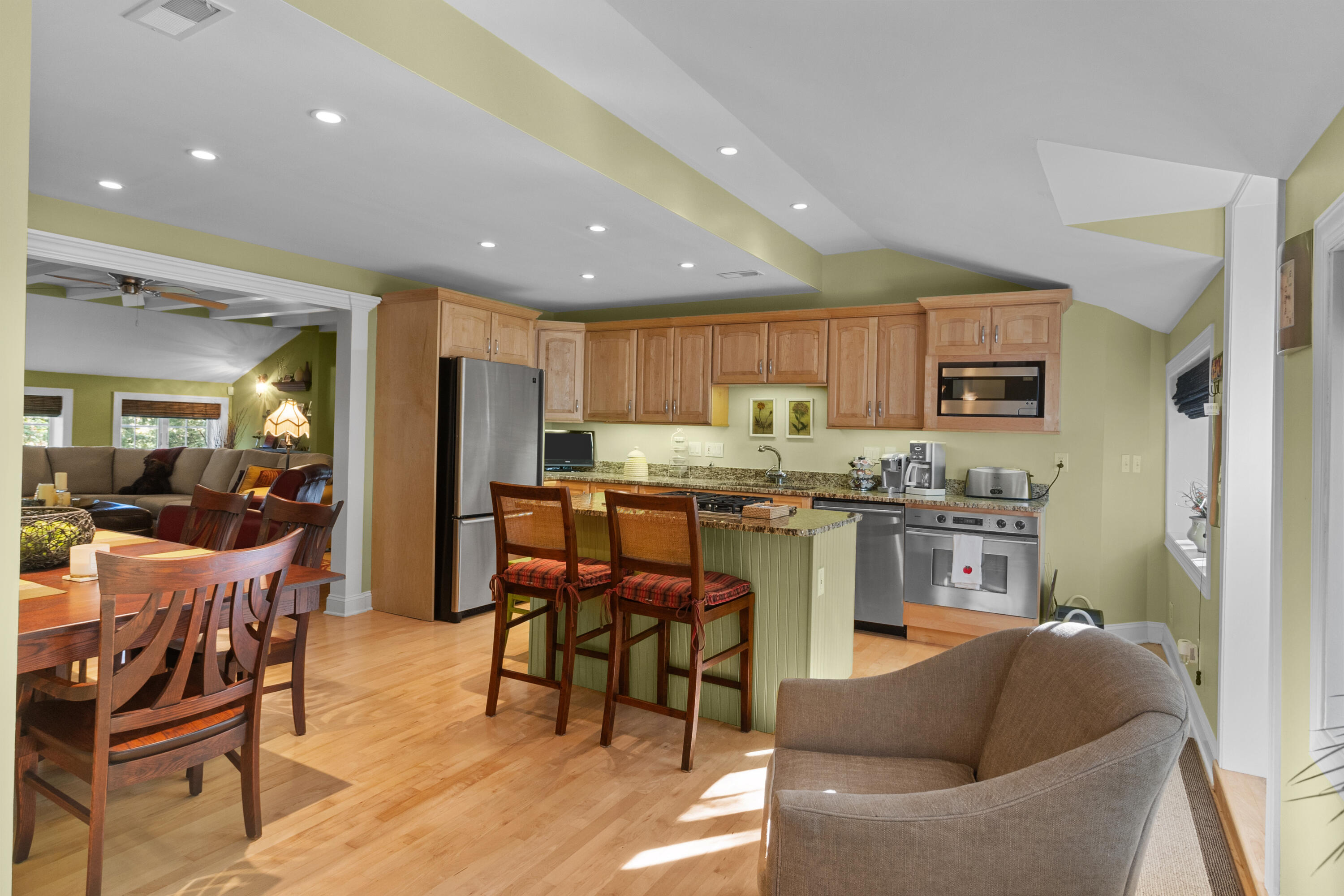 Open-plan kitchen with granite island, wooden cabinets, stainless appliances, and dining area.