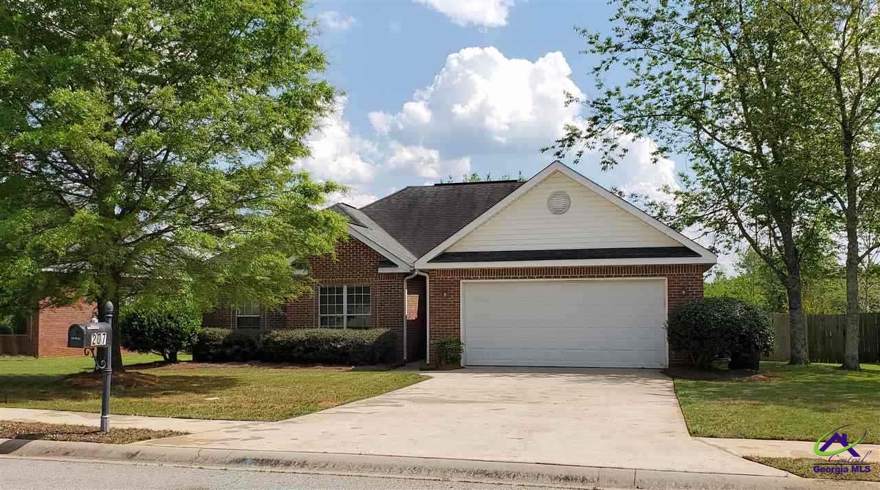 Red brick house with a white double garage, broad driveway, and mature trees.