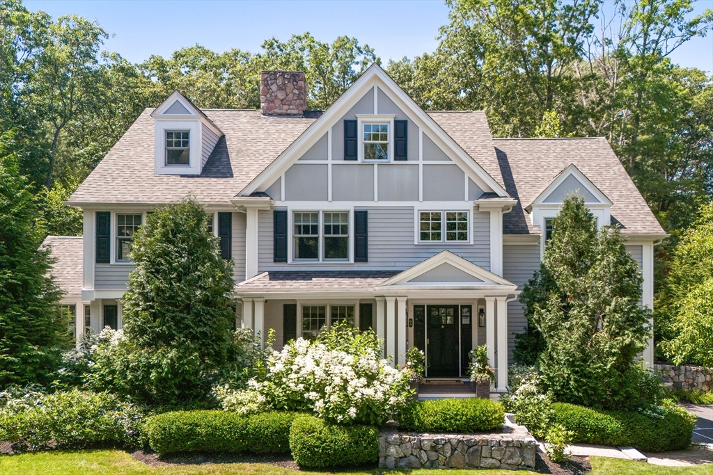 Gray multi-gabled home with dark shutters, a stone chimney, and landscaped front garden.