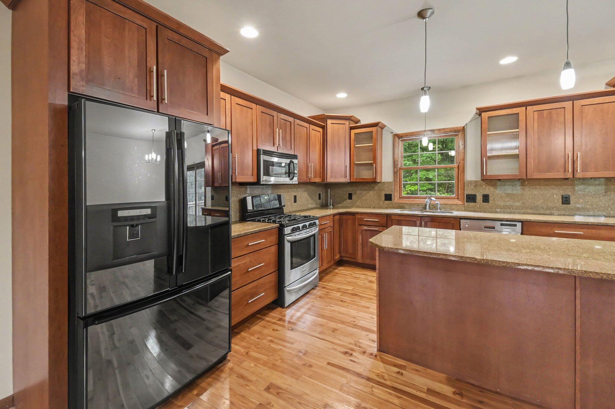 Kitchen with wood cabinets, hardwood floors, granite island, and a window above the sink.
