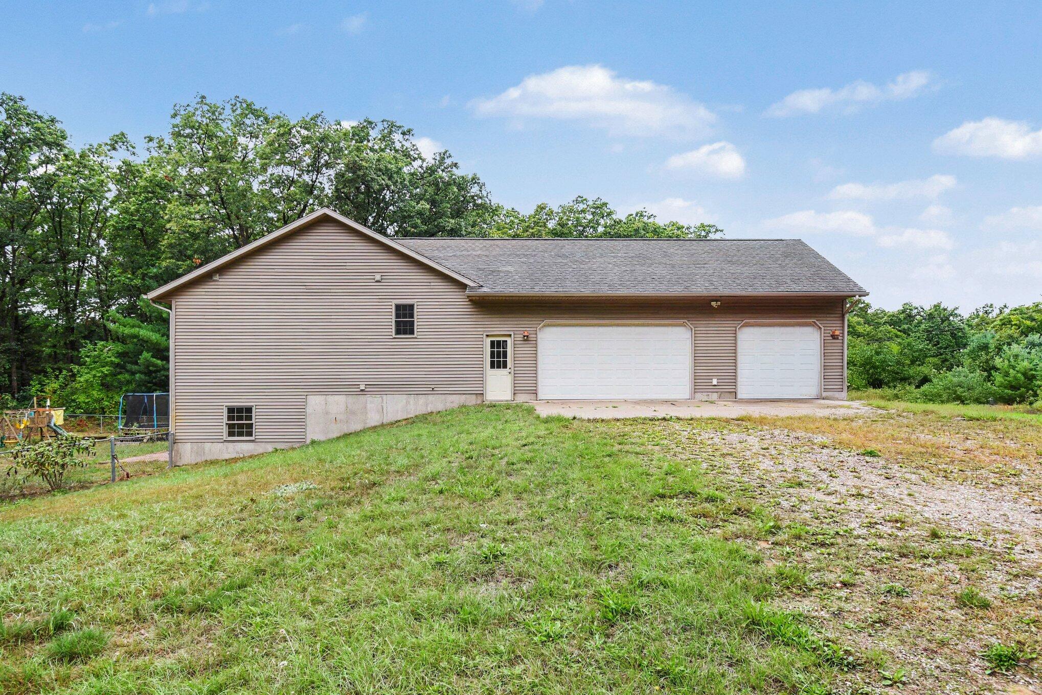 Beige-sided house with two white garage doors and a gravel-and-grass driveway.