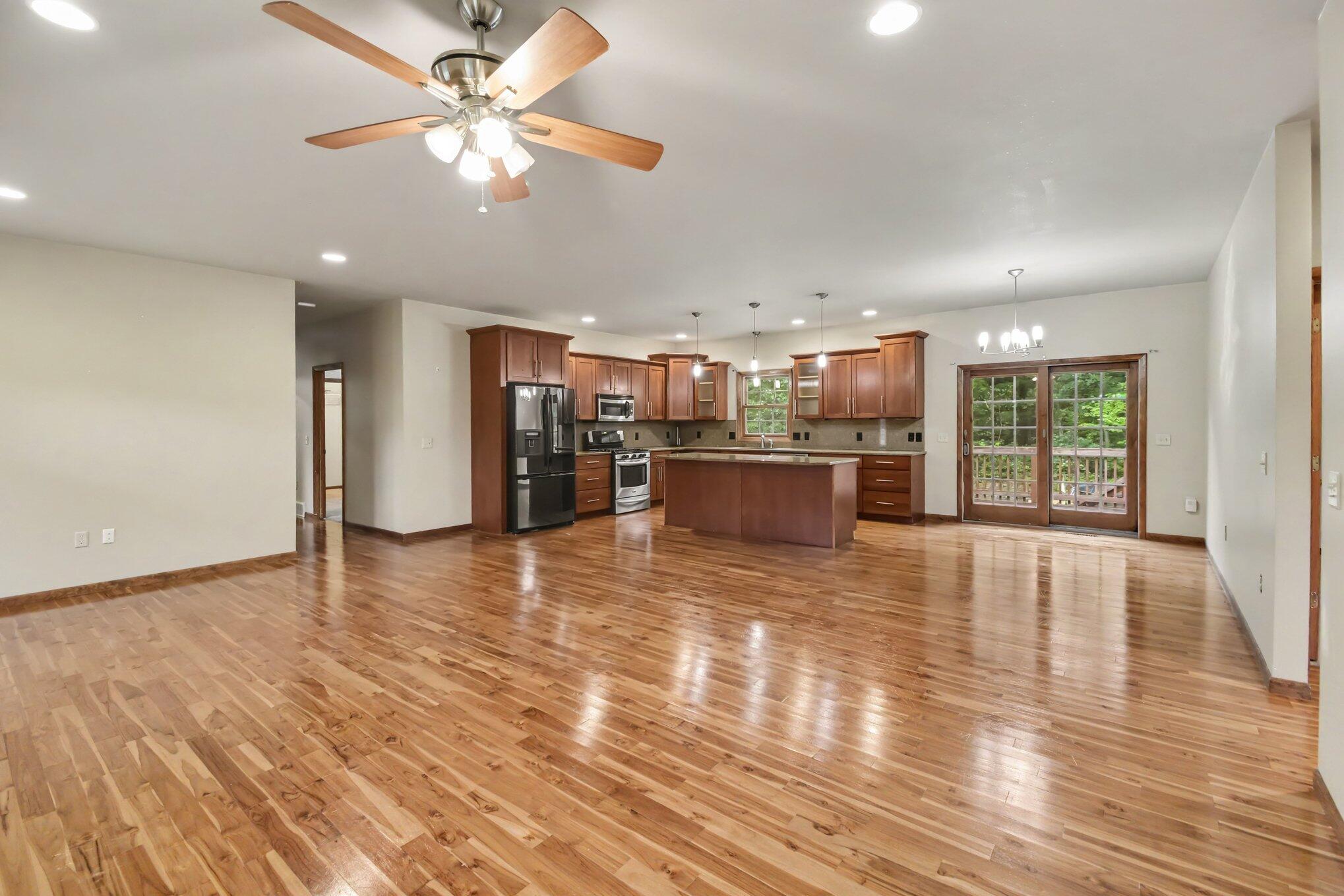 Open kitchen and living area with a central island, hardwood floors, stainless appliances, and deck doors.