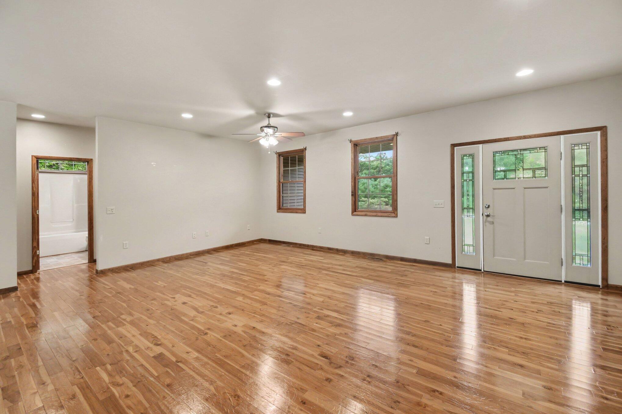 Vacant room with polished hardwood floors, wood-trimmed windows, and a glass-paneled front door.