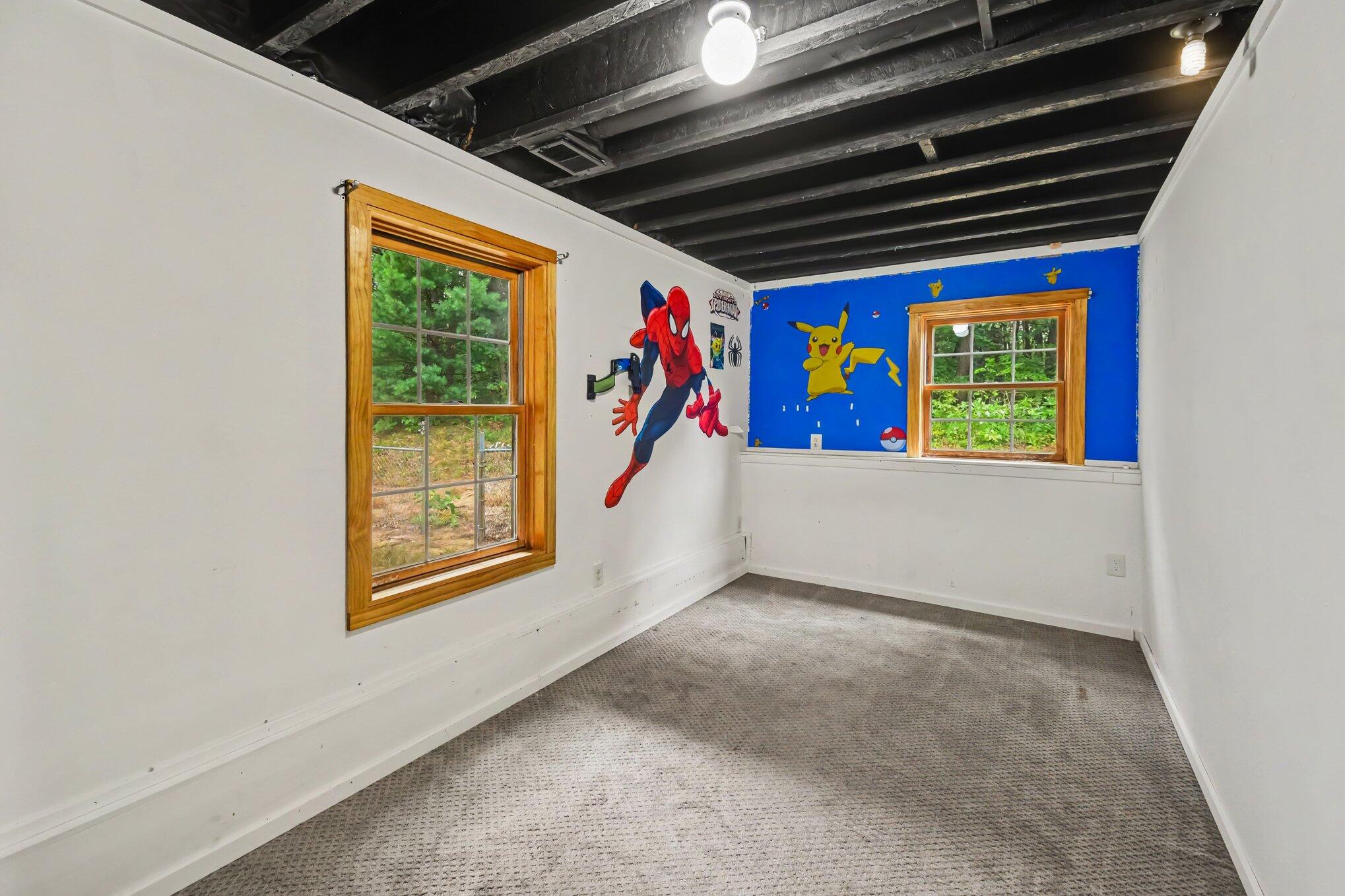 Empty carpeted room with Spider-Man and Pikachu wall decorations, two windows, and exposed ceiling beams.