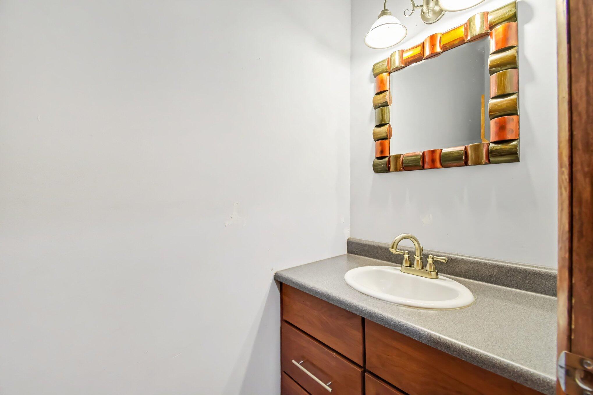 Bathroom vanity with an oval sink, gray countertop, brass-tone faucet, and colorful framed mirror.