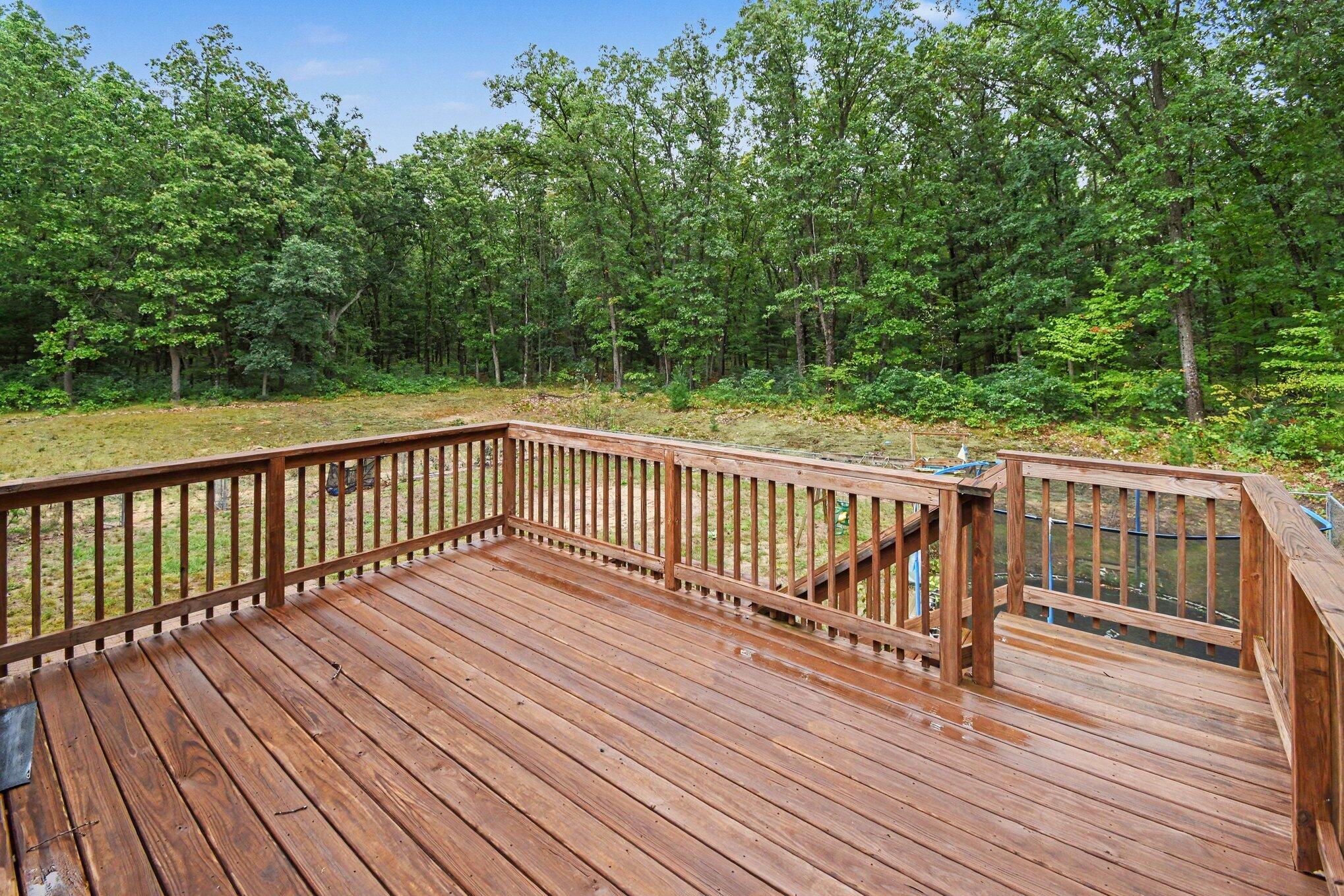 Wooden backyard deck overlooking an above-ground pool and dense trees.