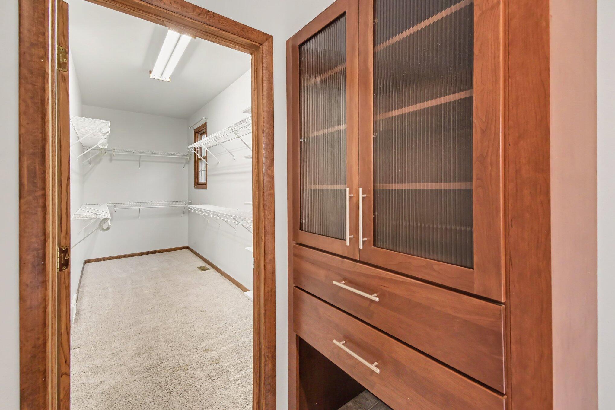 Walk-in closet with wraparound wire shelving and a cherry-wood cabinet with ribbed-glass doors.