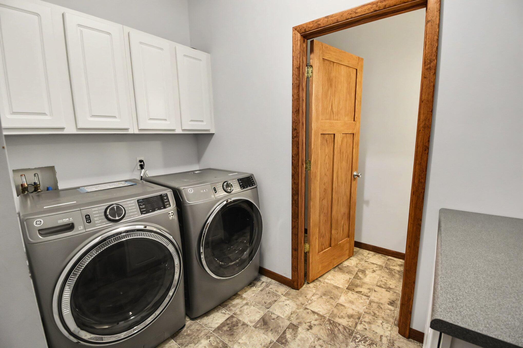Laundry room with front-loading washer and dryer, white cabinets, and a wood-trimmed doorway.