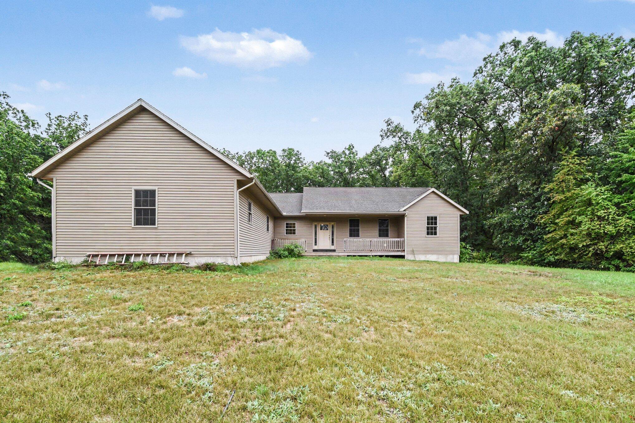 House rear exterior with beige siding, a covered porch, and a broad grassy yard.