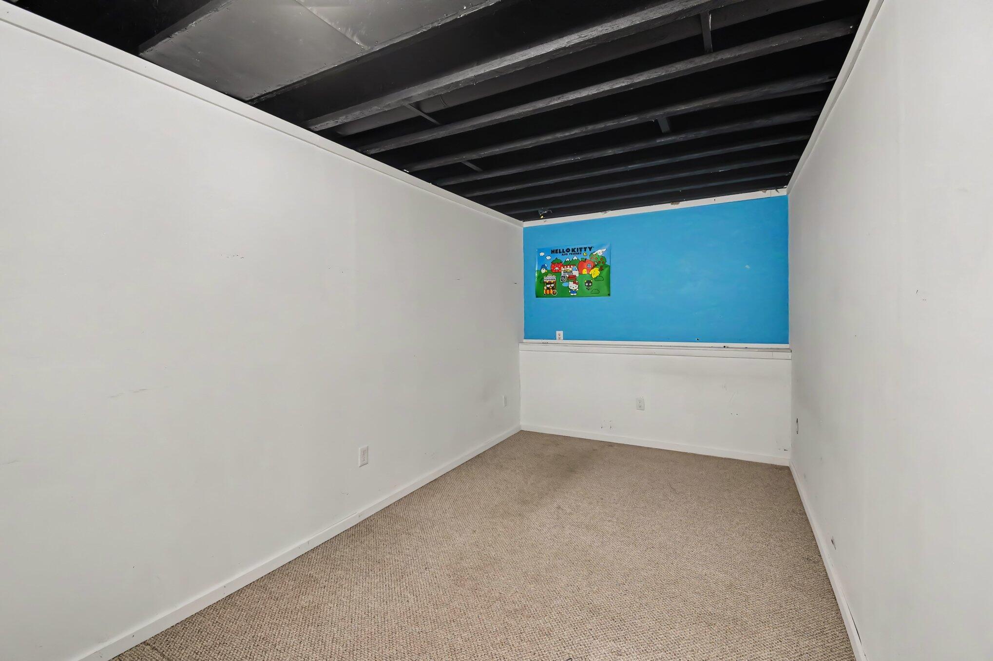 Empty carpeted room with exposed ceiling joists and a blue wall with a Hello Kitty poster.