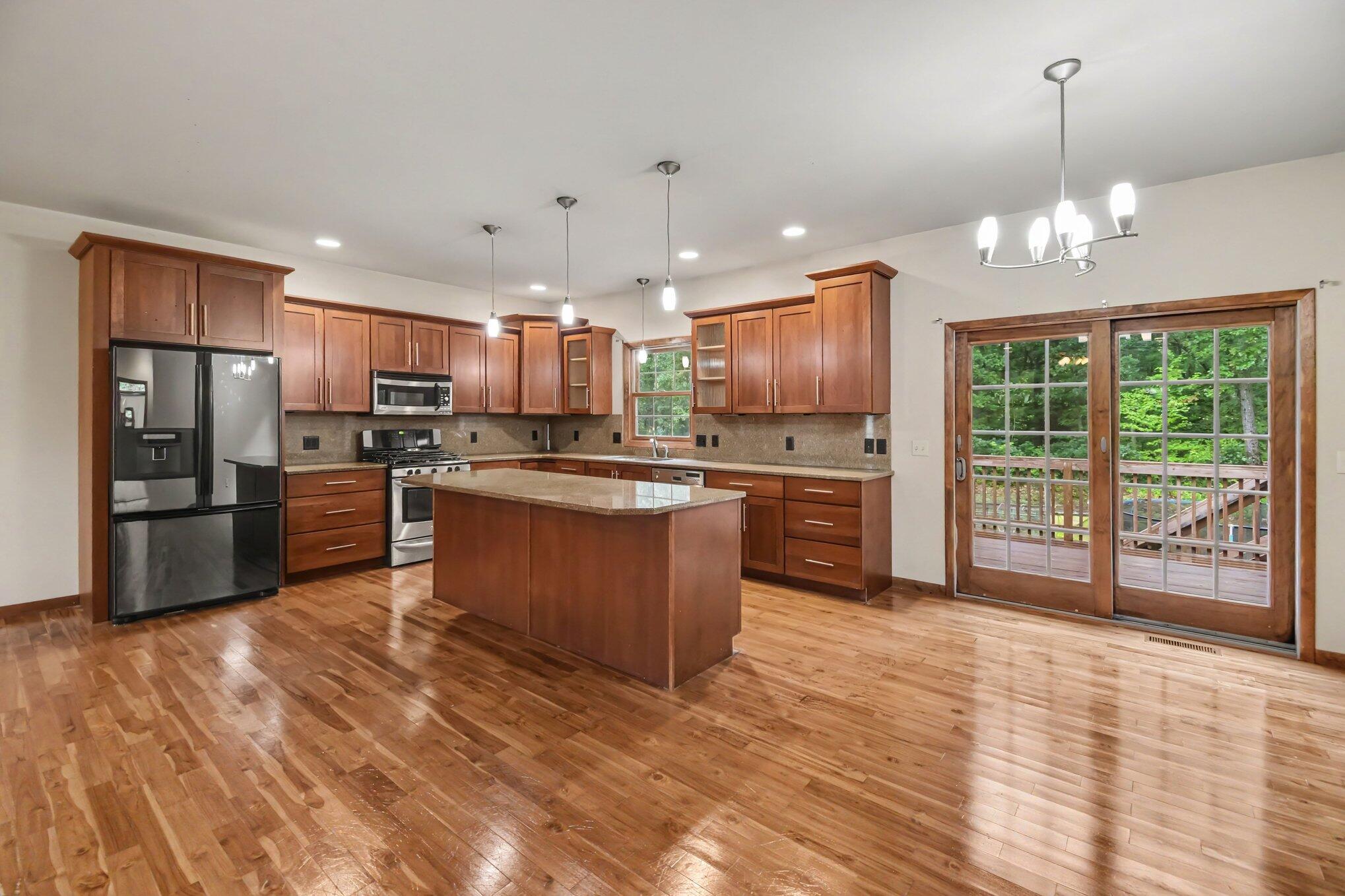Kitchen with a central island, wood cabinetry, hardwood floors, and glass doors to a tree-lined deck.