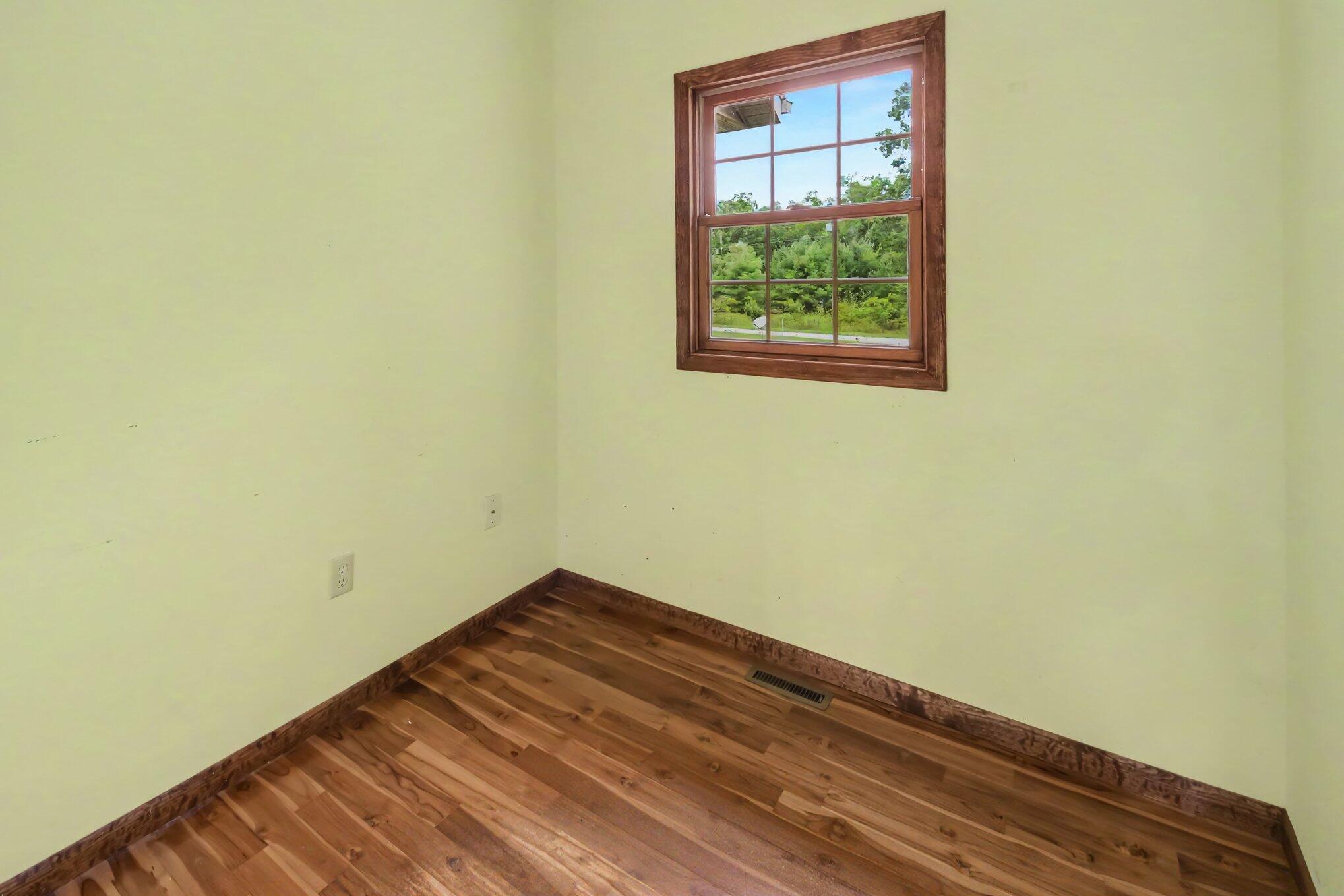 Empty room with wood flooring, pale yellow walls, and a wood-trimmed window.