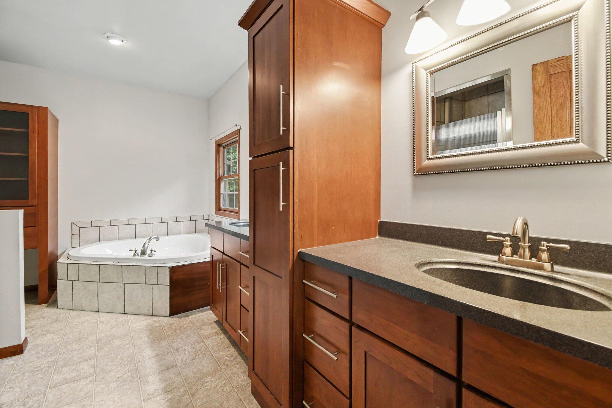 Bathroom with a tiled corner soaking tub, wood cabinetry, and a dark countertop vanity.
