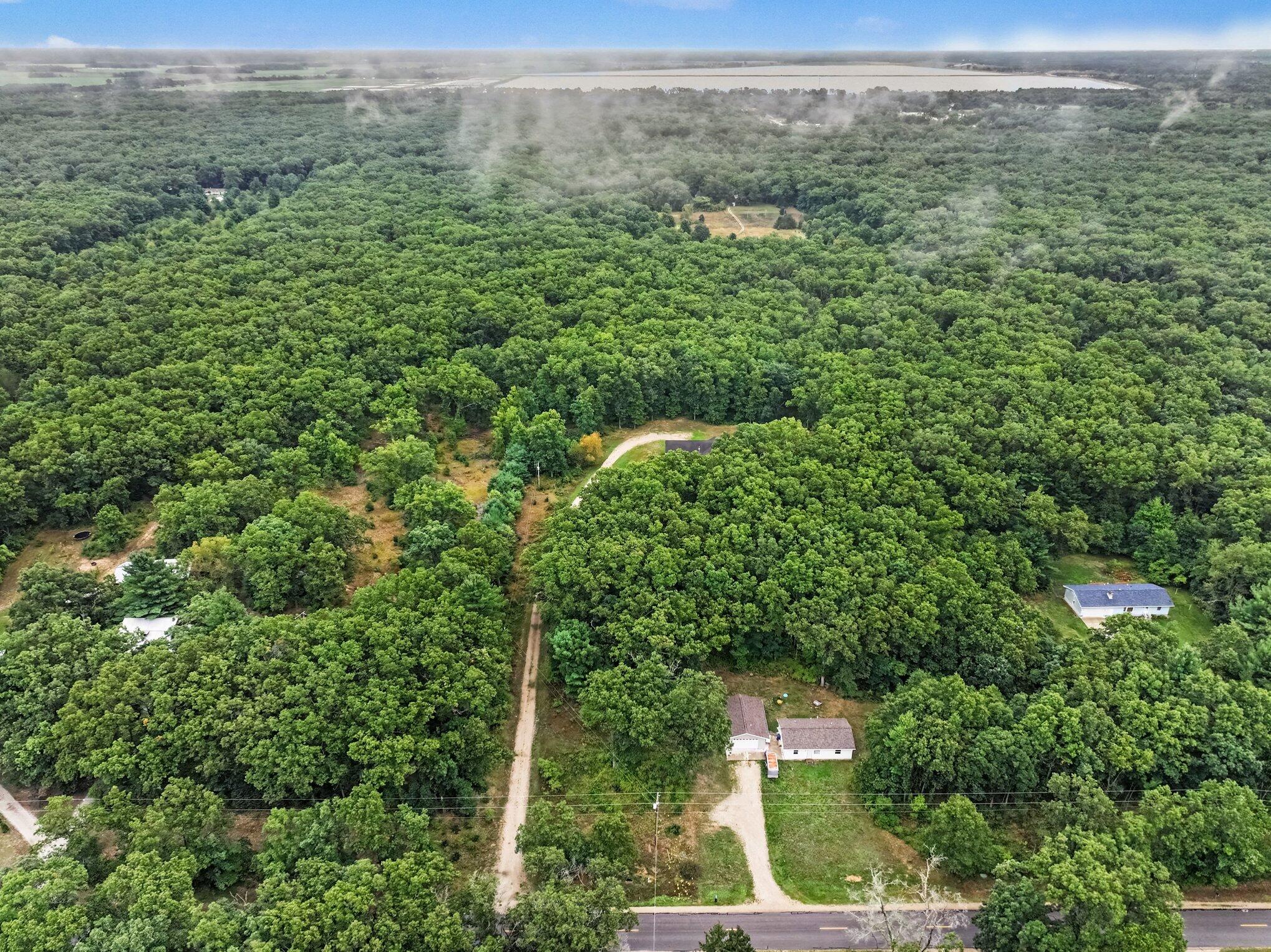 Aerial view of wooded property with scattered homes, dirt driveways, and water in the distance.