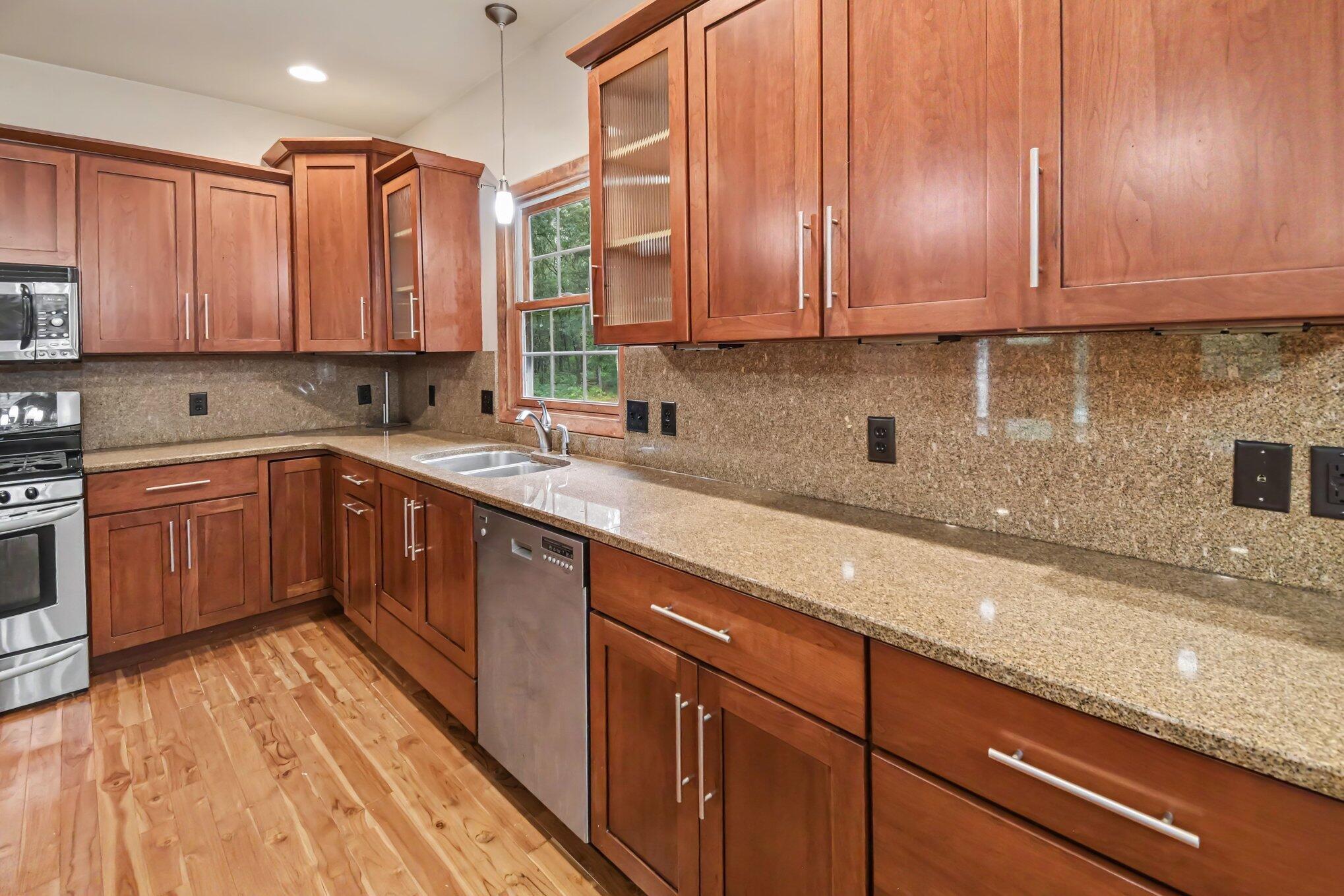 Kitchen with reddish wood cabinets, granite counters, stainless steel appliances, and a sink beneath a window.