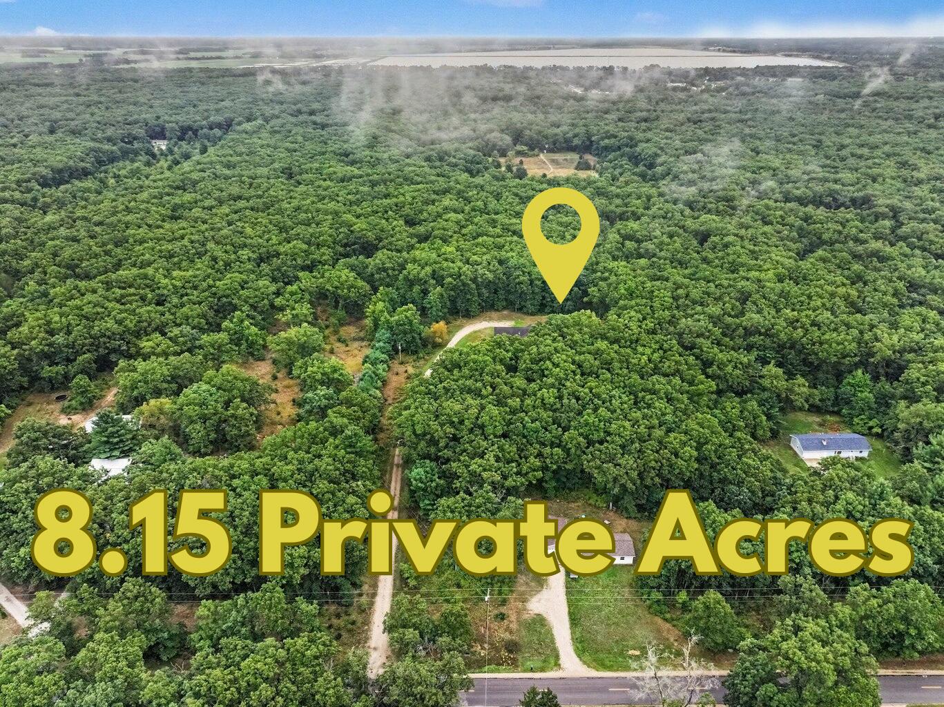 Aerial view of wooded 8.15-acre property with an access road and yellow location marker.