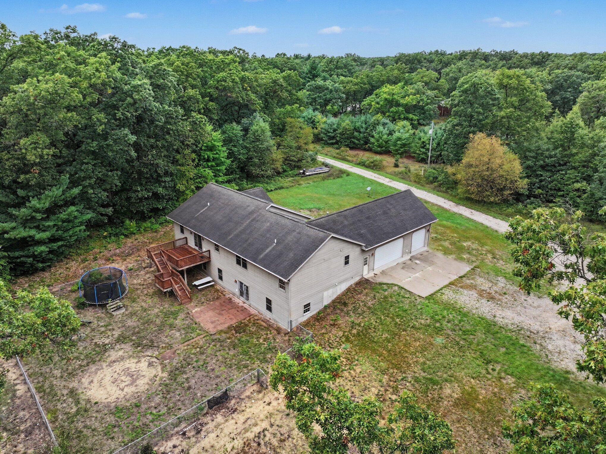 Aerial view of a house surrounded by trees, with an attached garage, wooden deck, and trampoline.