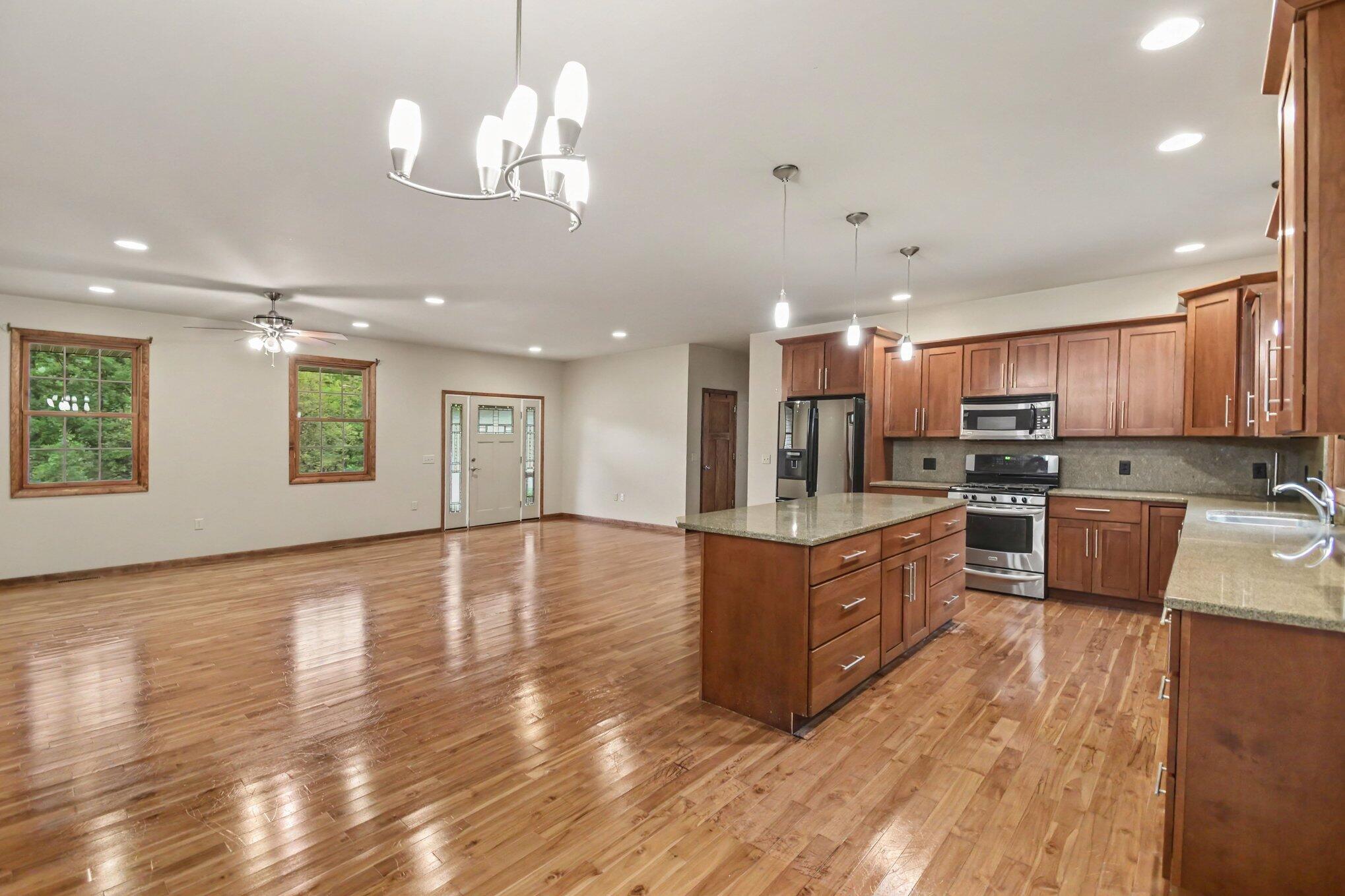 Open kitchen with a granite island, wood cabinetry, stainless steel appliances, and adjoining hardwood-floored dining area.
