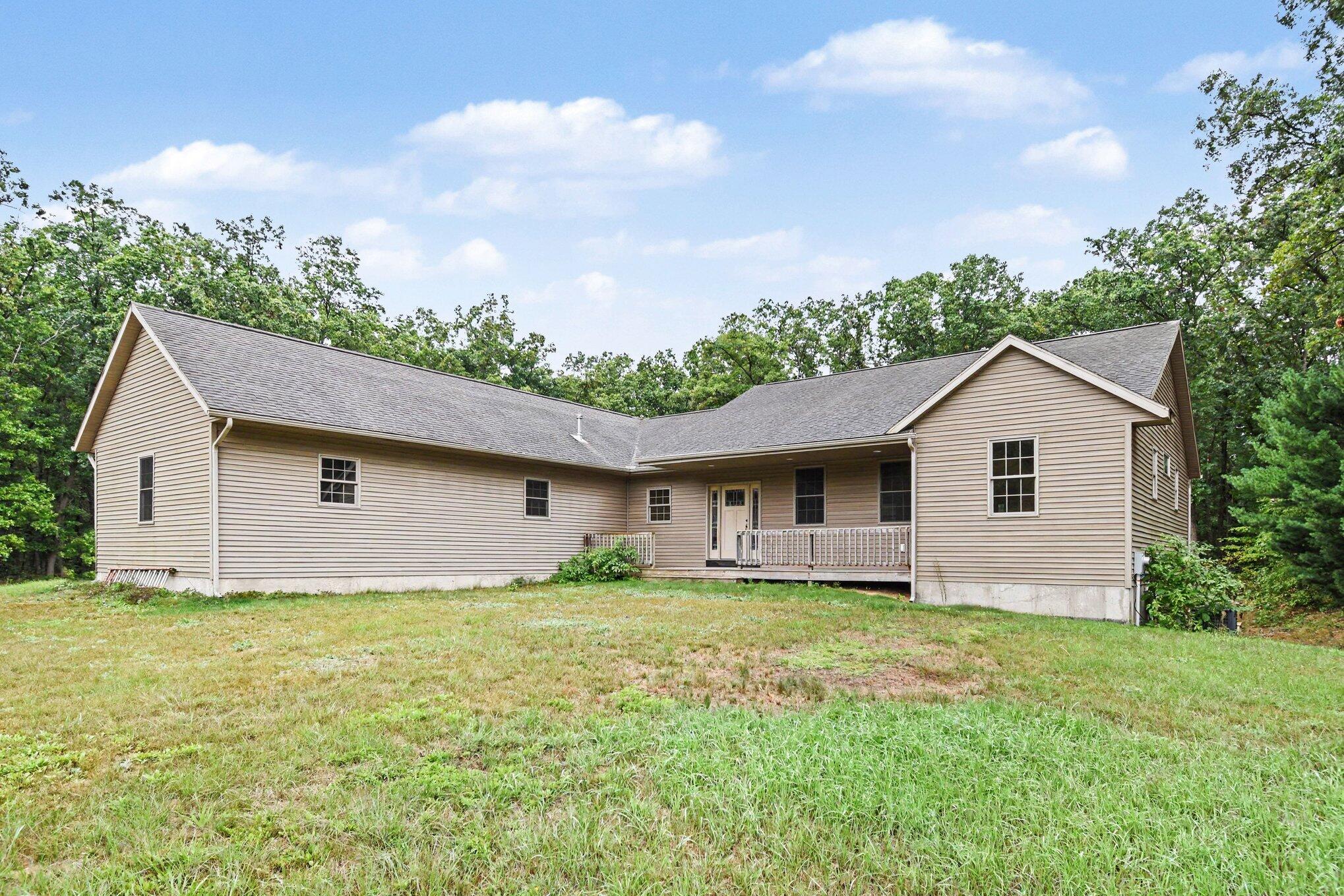 Beige single-story house with a covered porch, broad grassy yard, and mature trees.