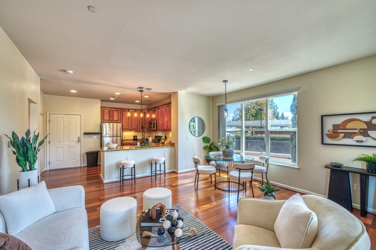 Open-plan living room with white sofas, hardwood floors, and a kitchen with warm wood cabinets.