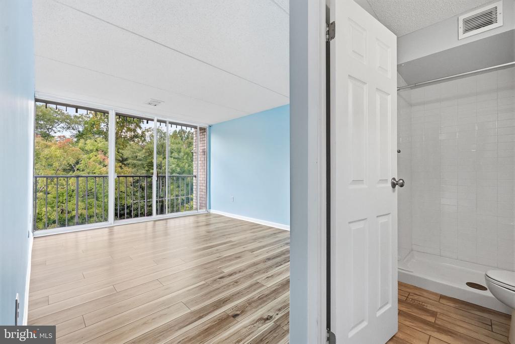 Vacant bedroom with sliding glass doors overlooking trees, beside an adjoining tiled bathroom.