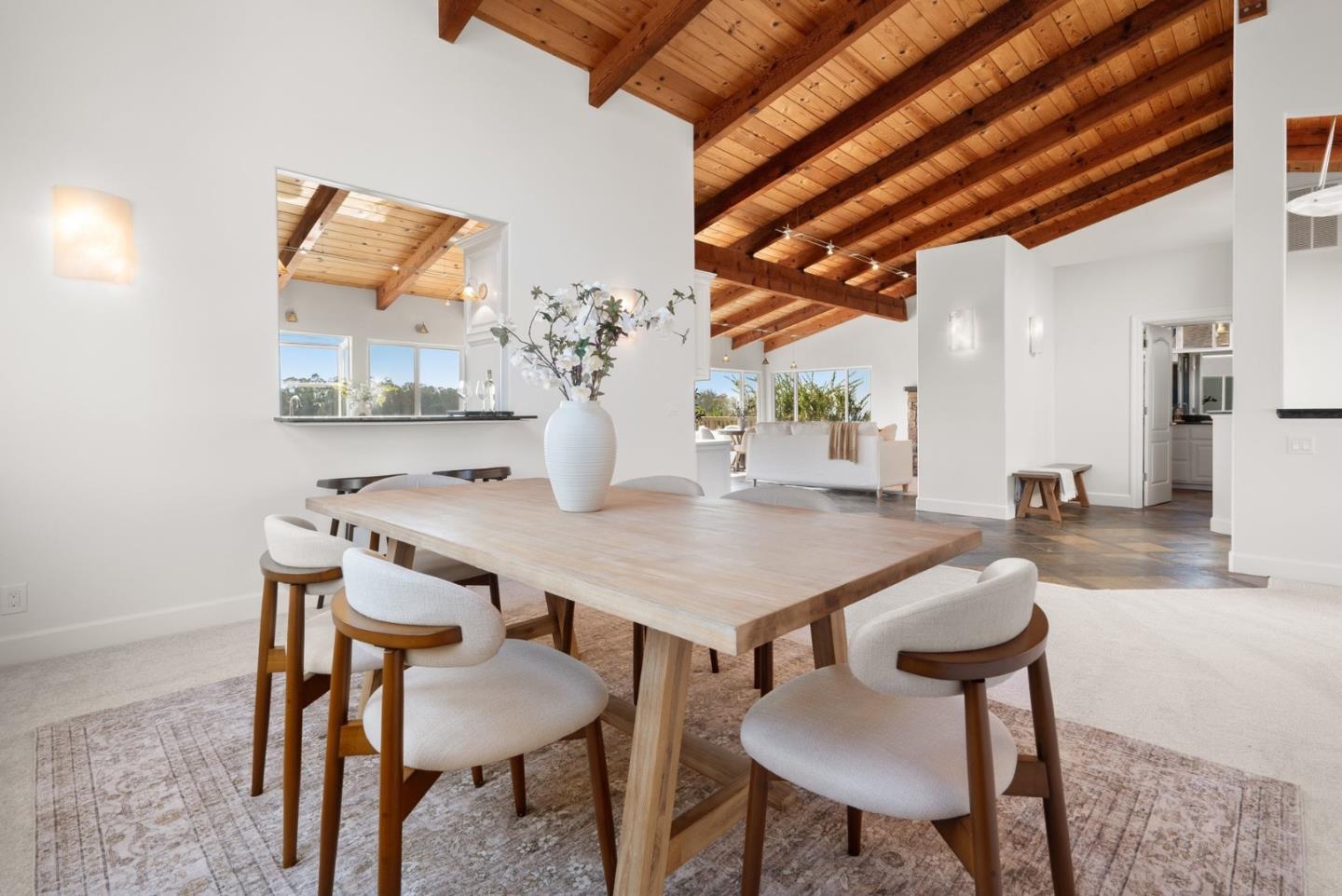 Dining room with a light-wood table beneath a vaulted exposed-beam ceiling, opening onto the living area.