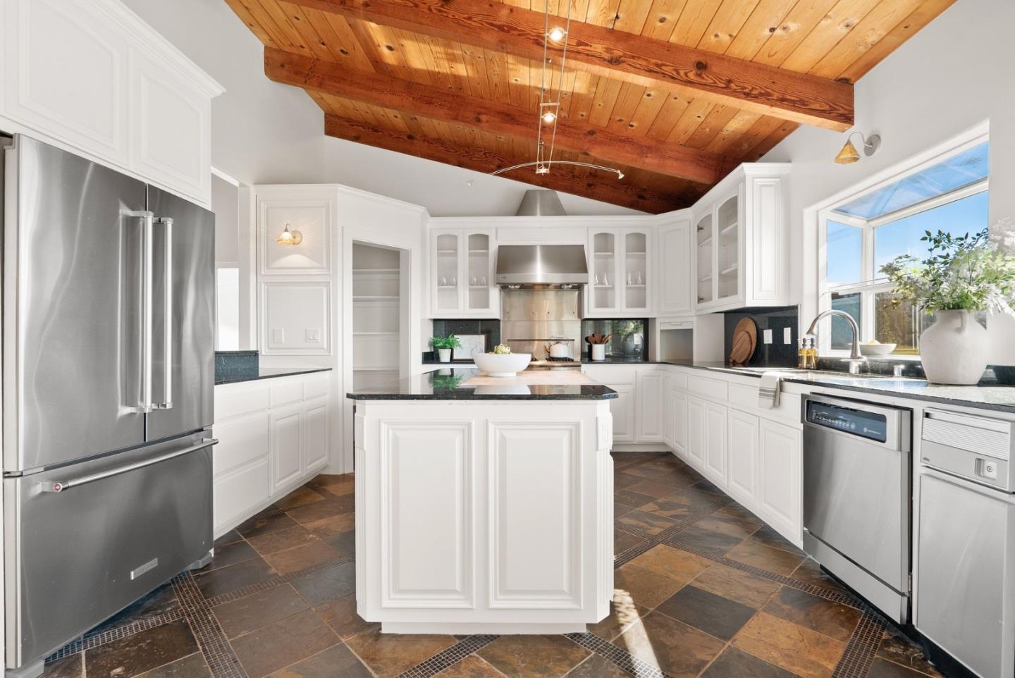 Kitchen with a central island, white cabinets, stainless steel appliances, and a vaulted wood ceiling.