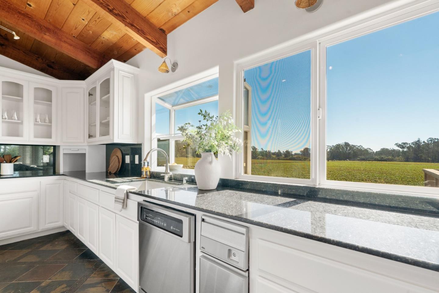 Kitchen with white cabinetry, dark stone counters, a wood ceiling, and windows overlooking a field.