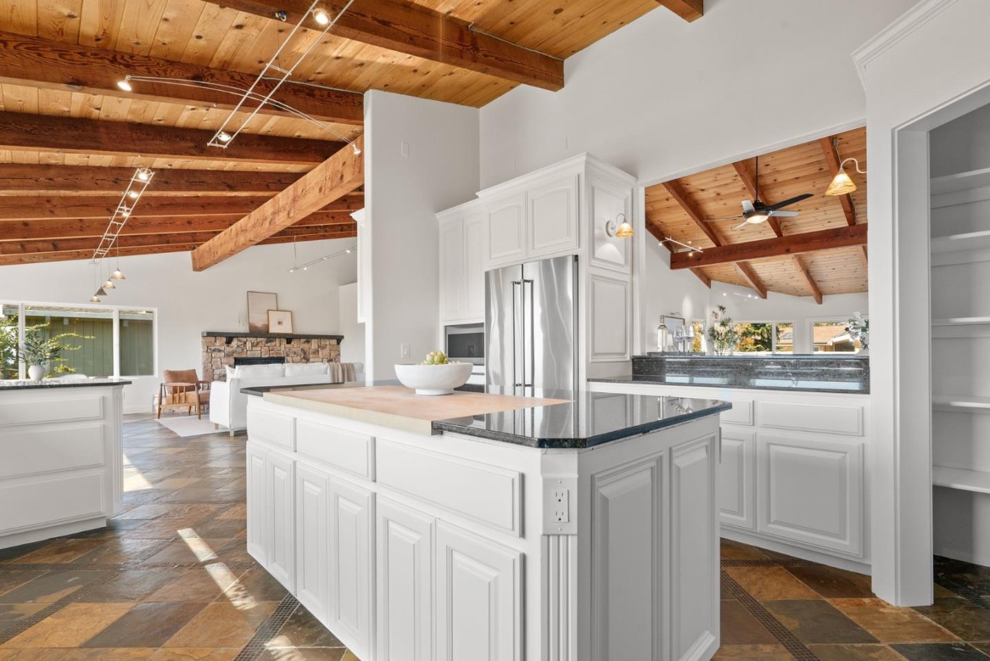 Open kitchen with a large white island, dark stone counters, and vaulted wood-beam ceiling.