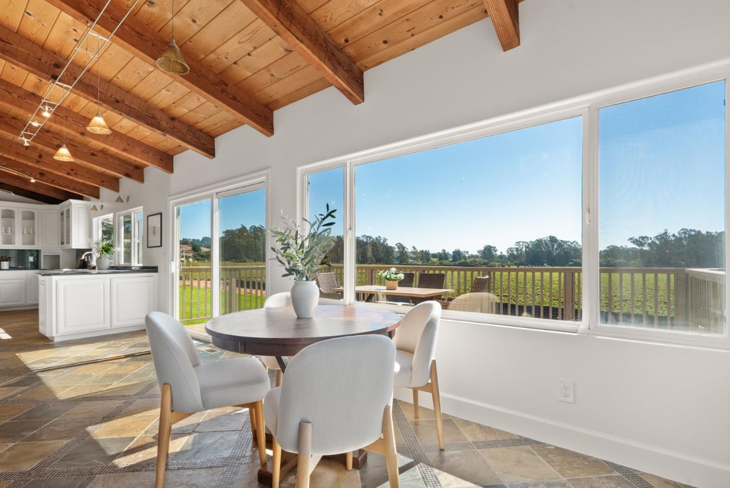 Dining area with vaulted wood ceiling and large windows overlooking green fields.